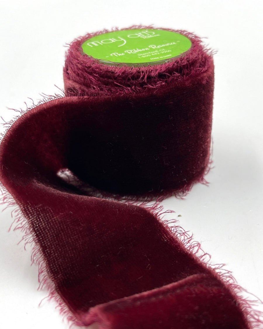 Roll of wine-colored silk velvet frayed ribbon with a loose length extending across a white background.