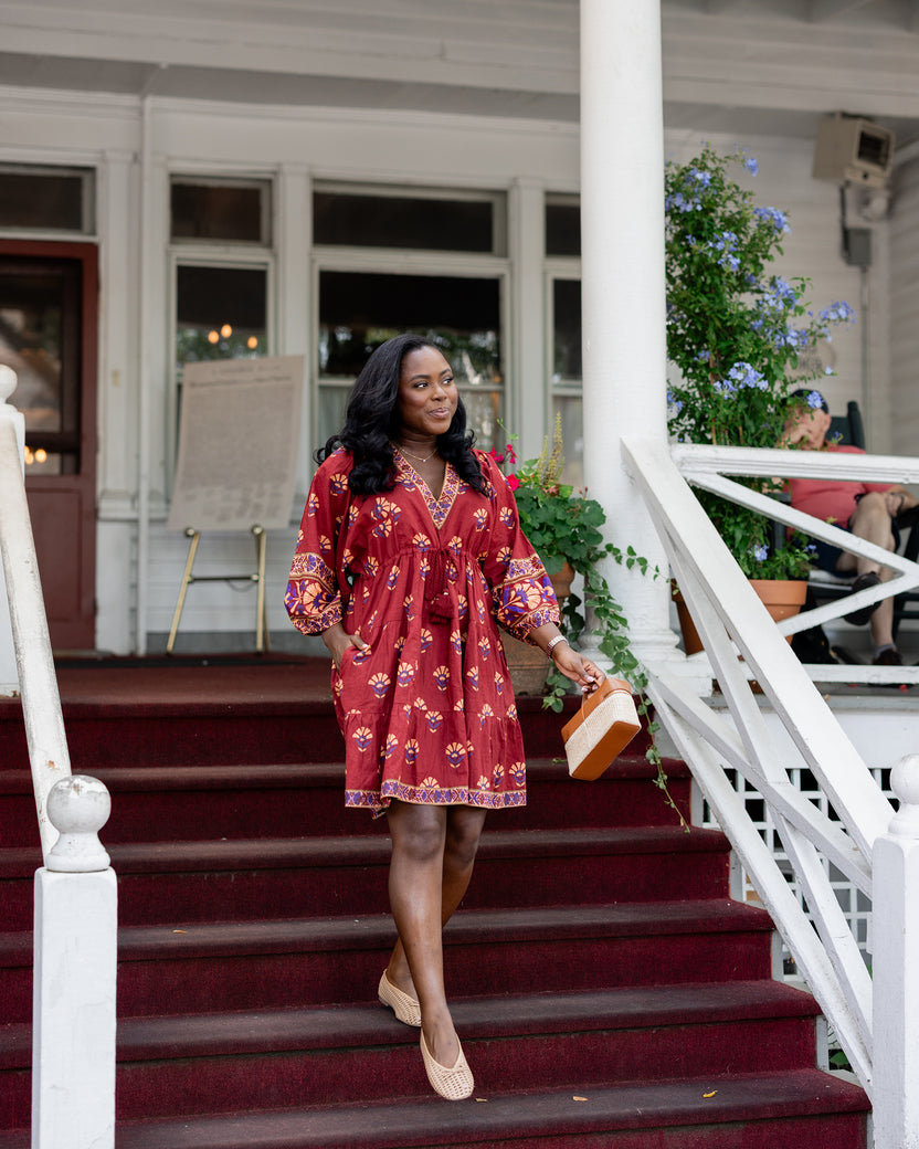Person wearing a red patterned knee-length dress while walking down carpeted steps.