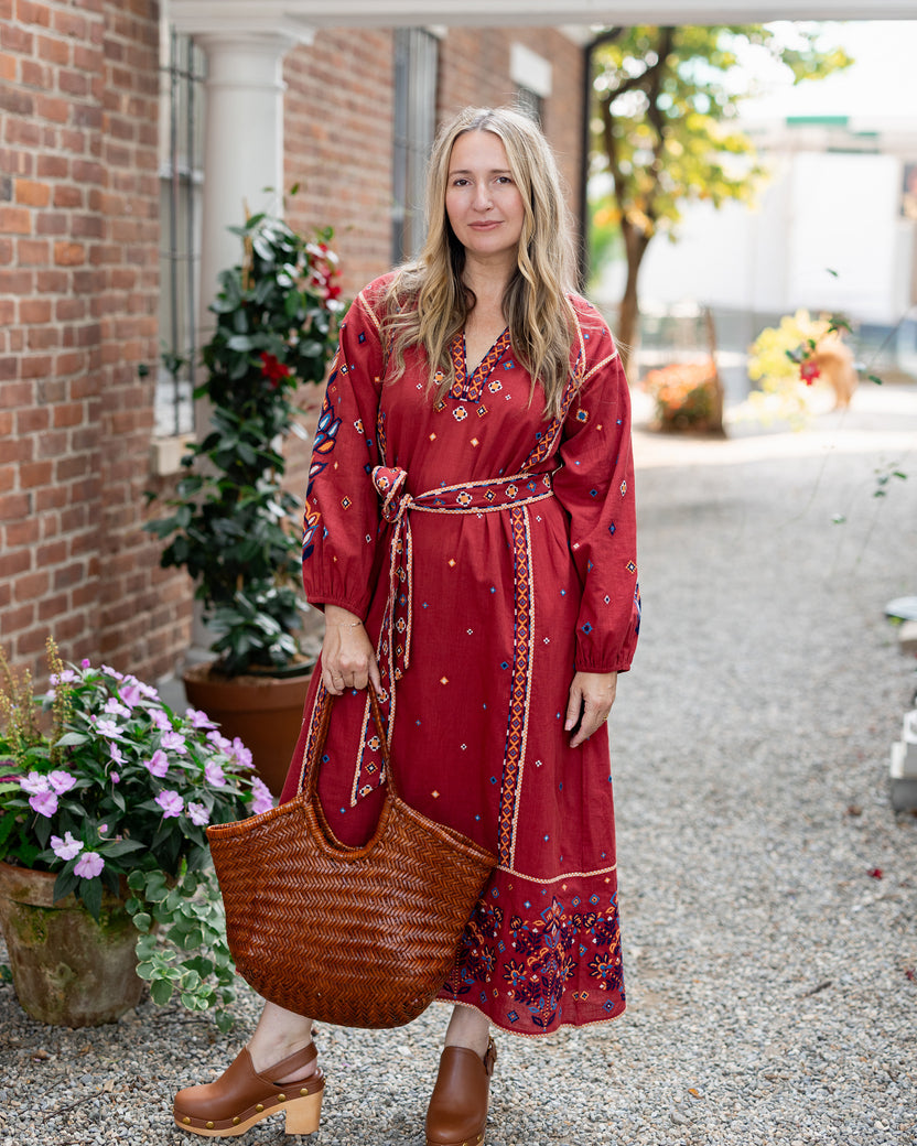 Person wearing a red patterned belted maxi dress and carrying a large woven tote outdoors.