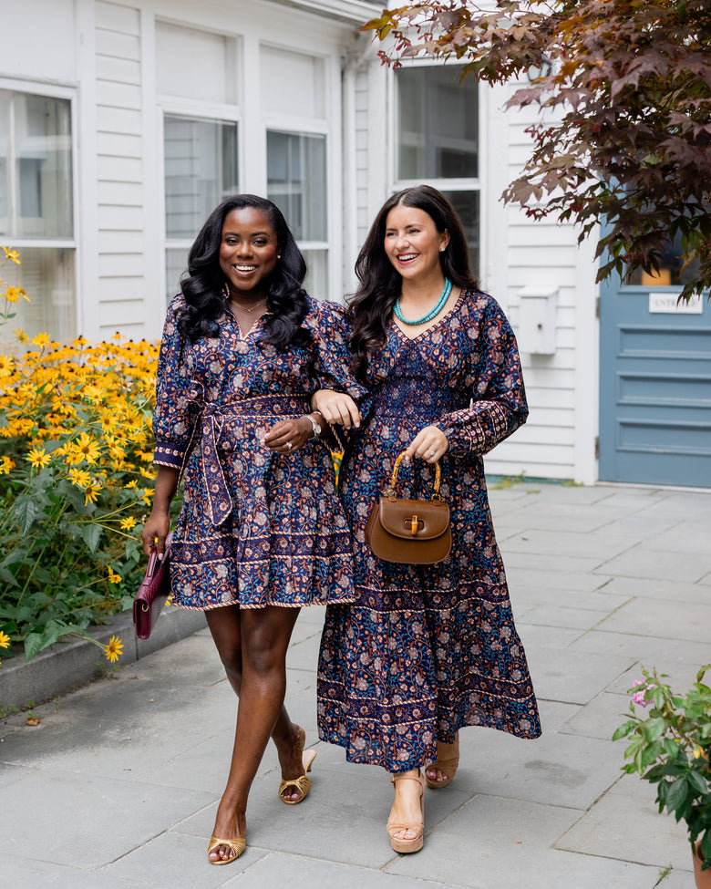Valley Garden Romy dress in a dark floral print with a turquoise necklace and brown handbag, shown outdoors.