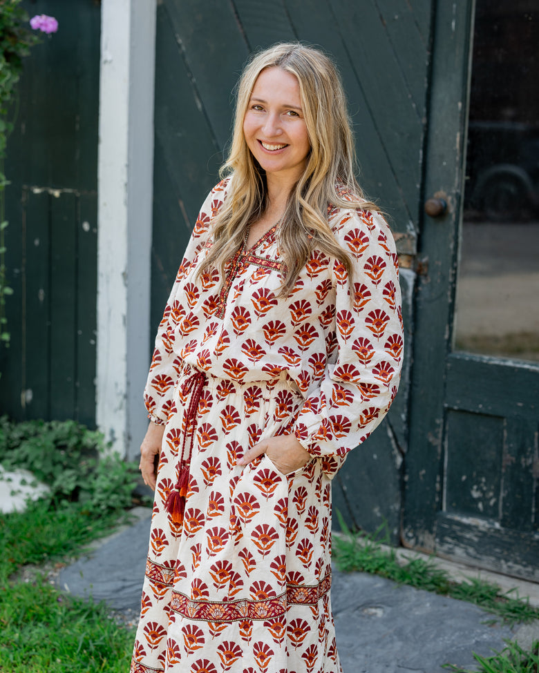 Person wearing a cream patterned blouse with a matching long skirt beside a dark barn door.
