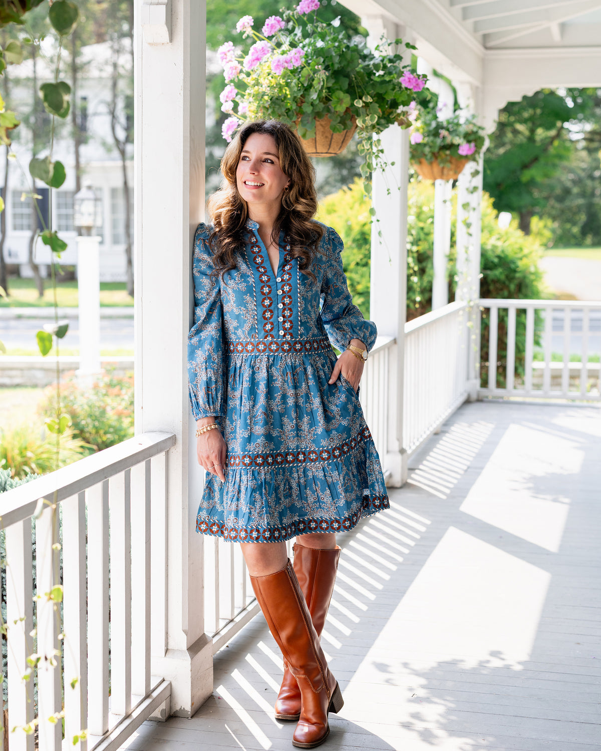 Person wearing a blue patterned above-the-knee dress with brown knee-high boots on a porch.