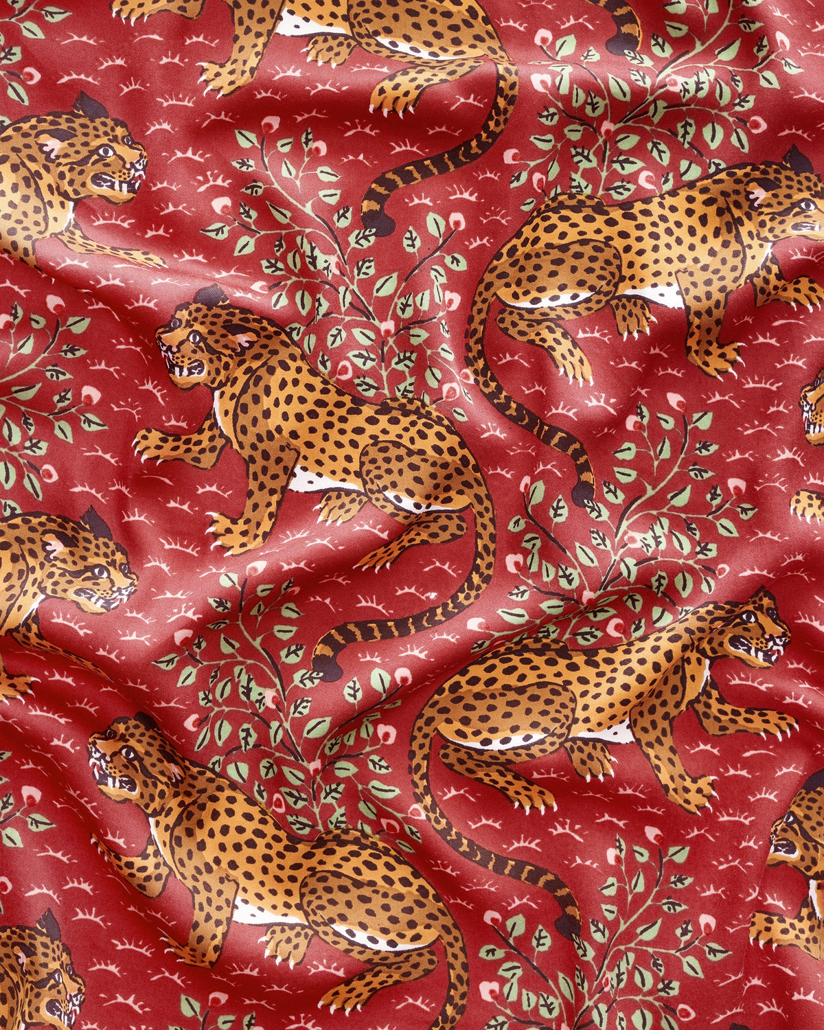 Close-up of the red fabric print with repeated spotted leopards, leafy branches, and small white motifs.