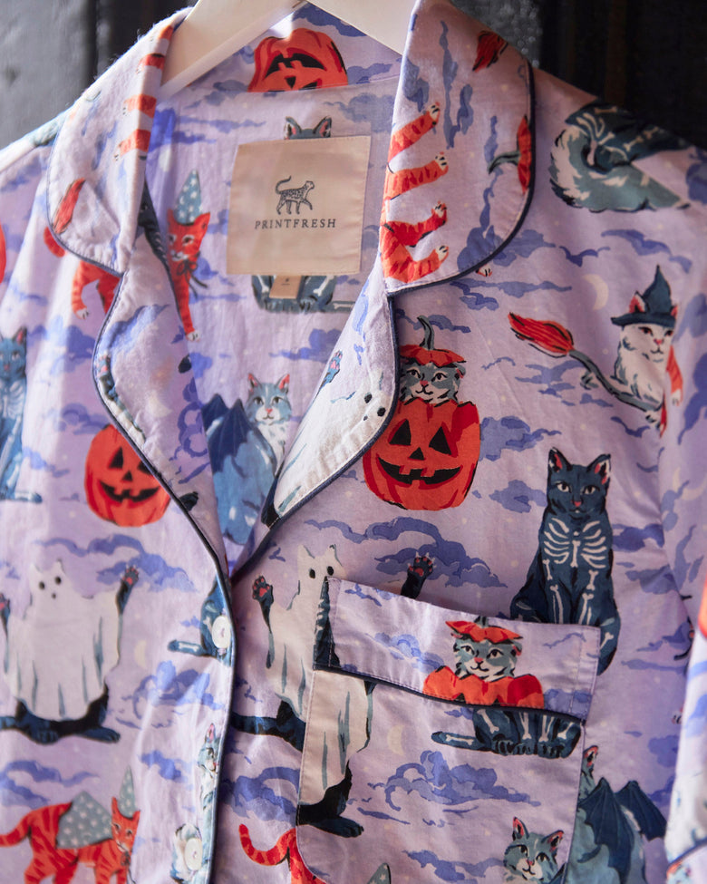 Close-up of the Halloween House Cats short pajama set showing the lavender cat-and-ghost print, notched collar, button front, chest pocket, and brand label.
