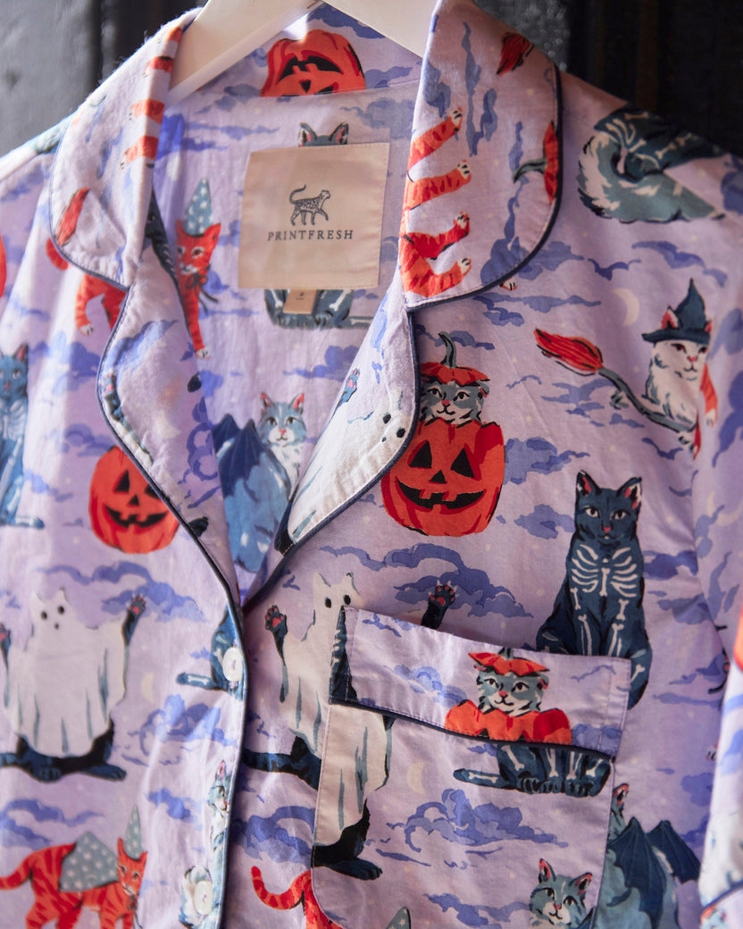 Close-up of the Halloween House Cats short pajama set showing the lavender cat-and-ghost print, notched collar, button front, chest pocket, and brand label.