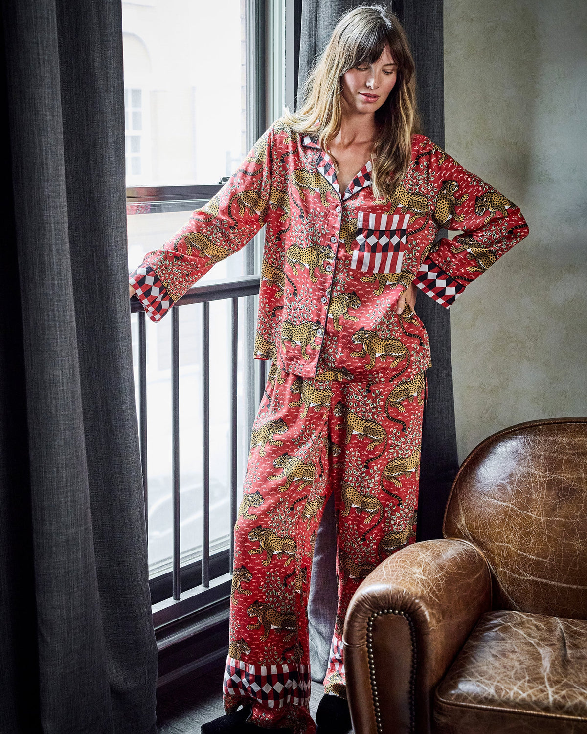 Model wearing the scarlet Bagheera satin pajama set, shown standing beside a window