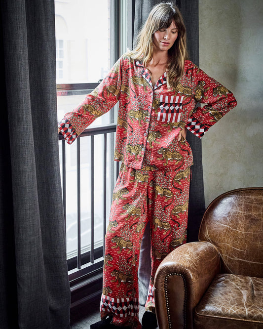 Model wearing the scarlet Bagheera satin pajama set, shown standing beside a window