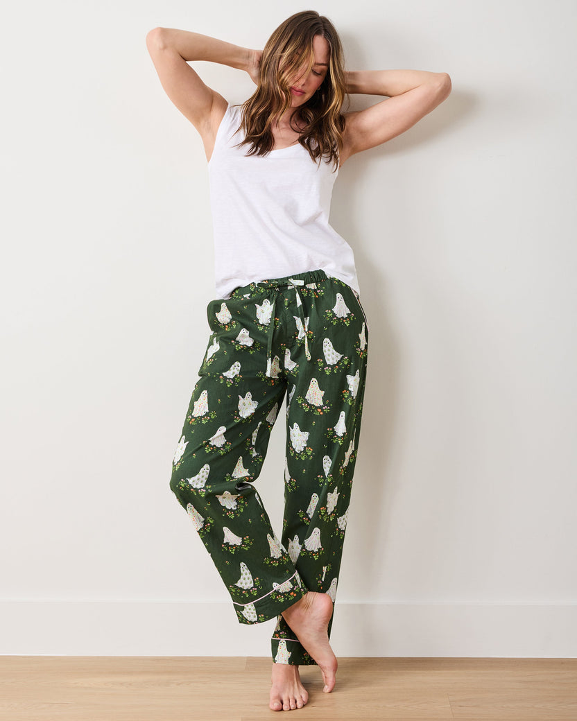 Model standing against a wall wearing dark green pajama pants with floral ghost prints and pink cuff piping.
