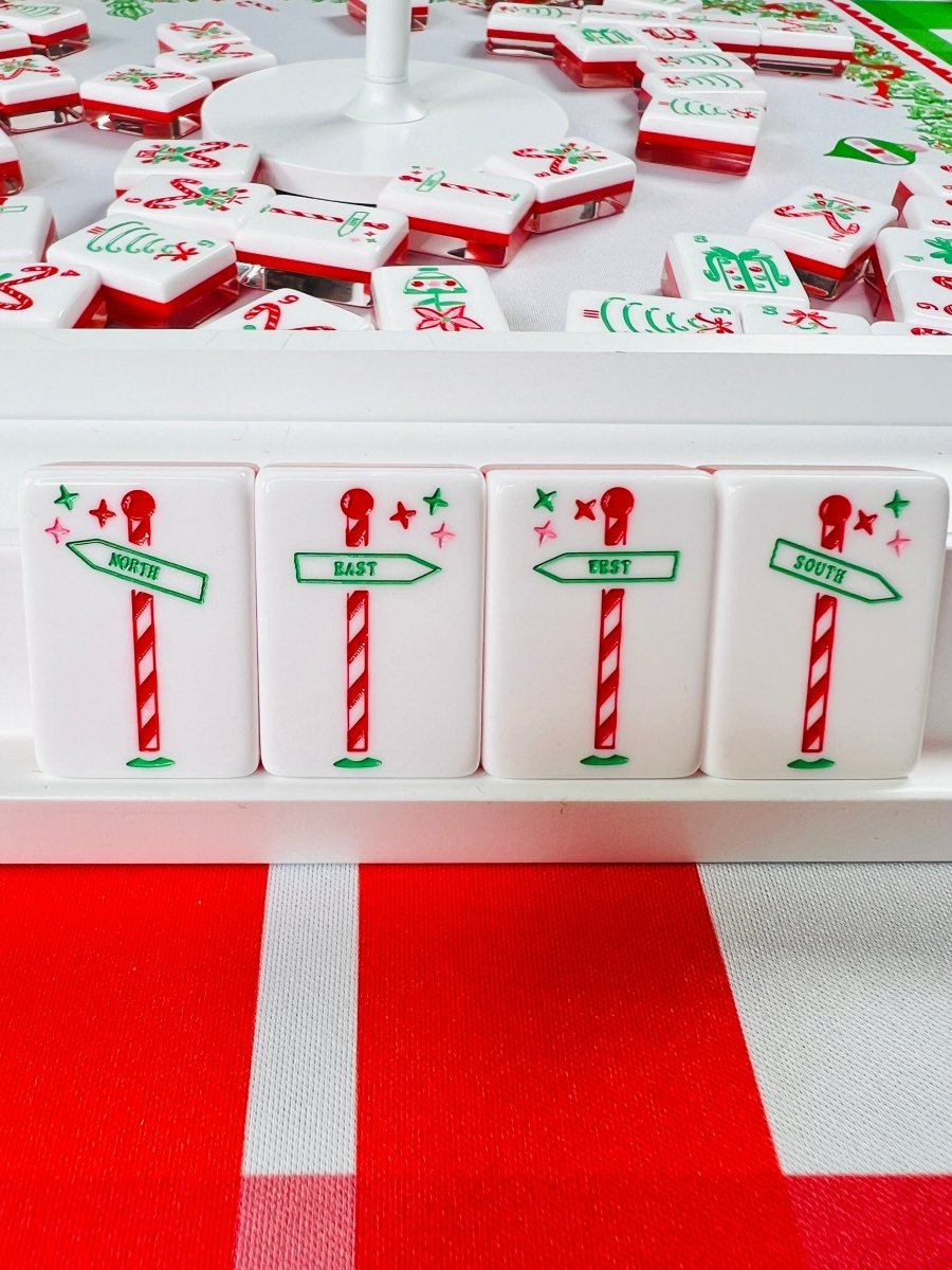 Front view of four holiday mahjong tiles showing candy-cane signpost designs labeled North, East, West, and South.