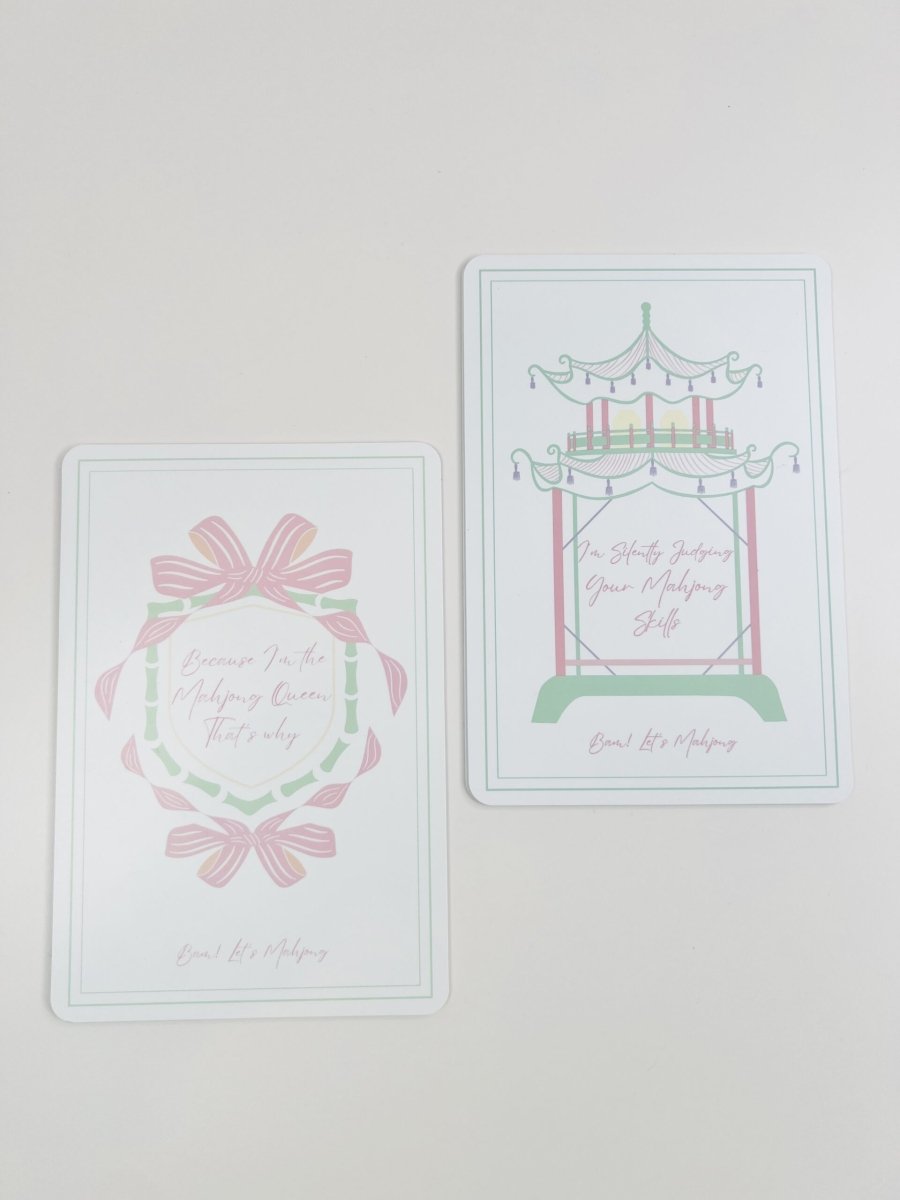 Two Mahjong tile shufflers shown together, one with a bow-and-wreath design and one with a carousel design, in pastel colors.