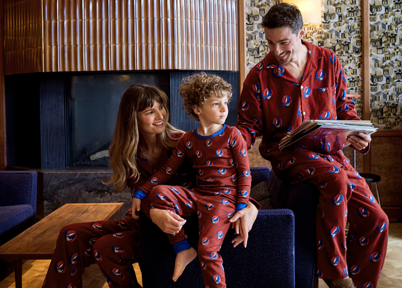 Three people seated together in matching red printed pajamas in a living room.